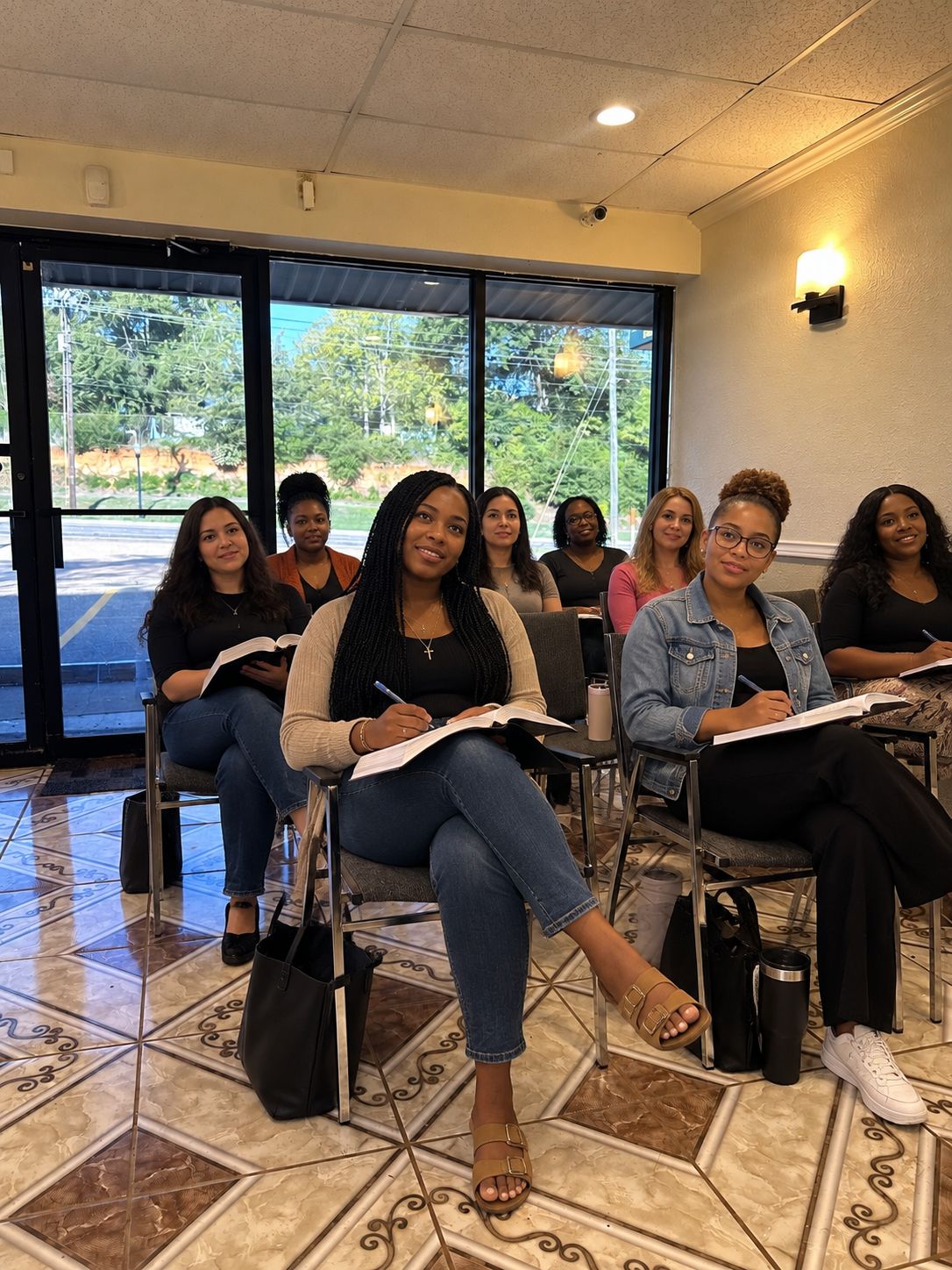 Young women seated together with open Bibles and notebooks, smiling toward the front of the room