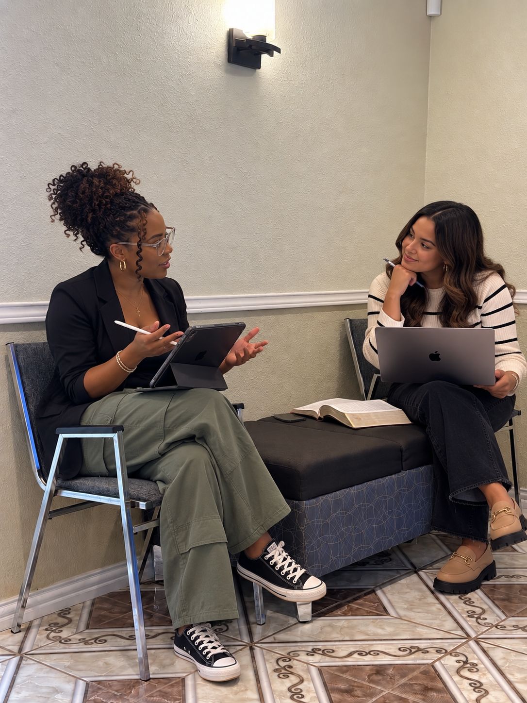 Two young women talking together, one with a tablet and one with a laptop and an open Bible between them